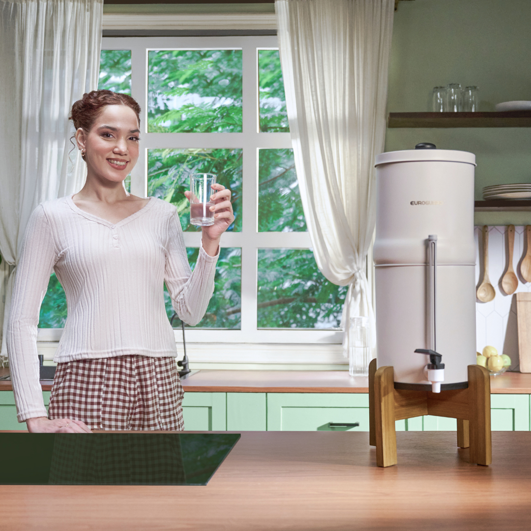 Woman holding a glass of water next to a water dispenser in a kitchen.